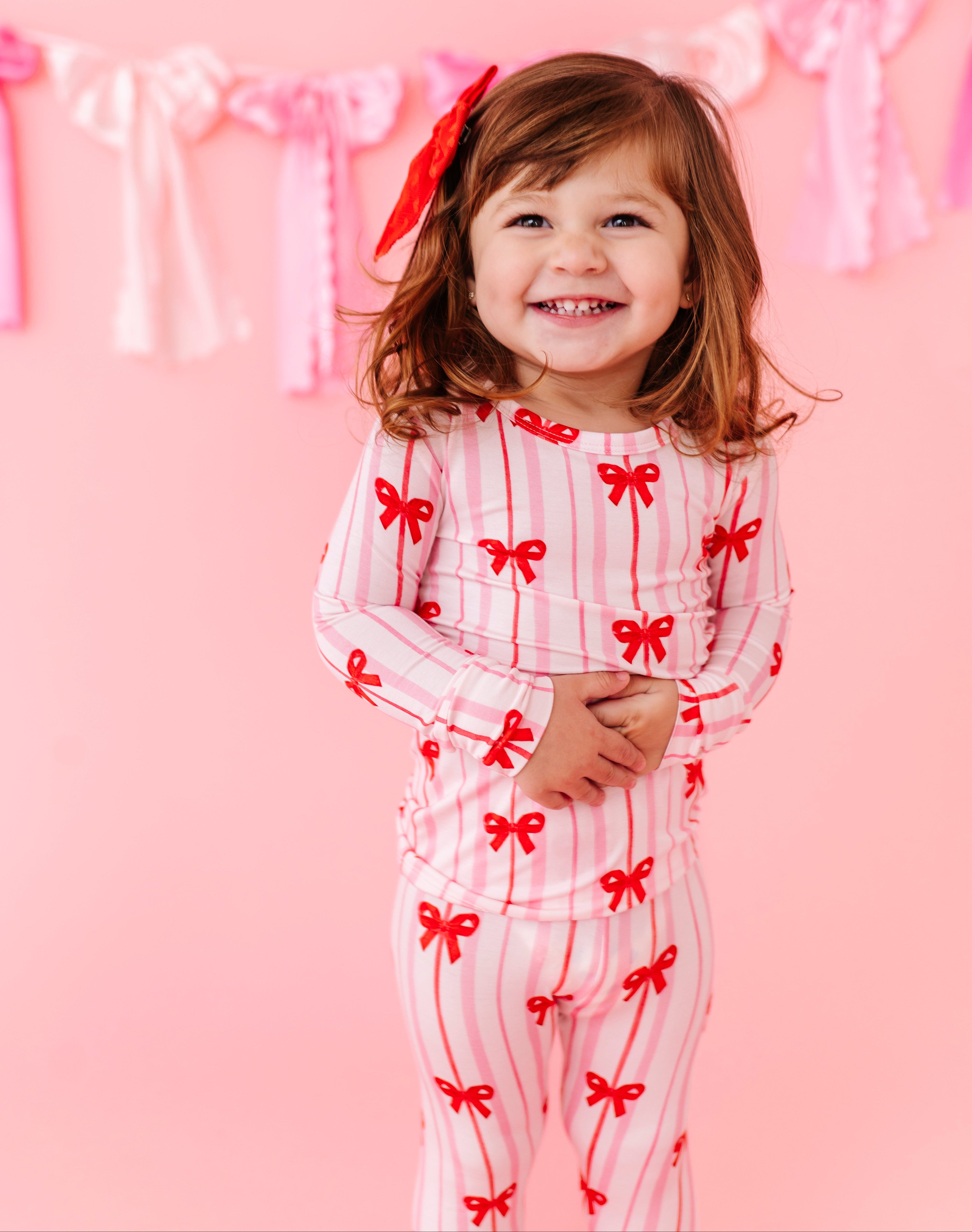 Toddler wearing Ruby Ribbons bamboo pajamas with red bow print and pink stripes